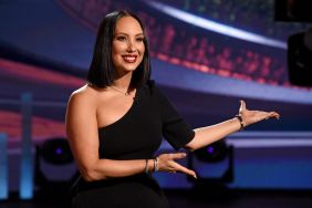 Cheryl Burke sitting in a black dress, holding her arms out to present something