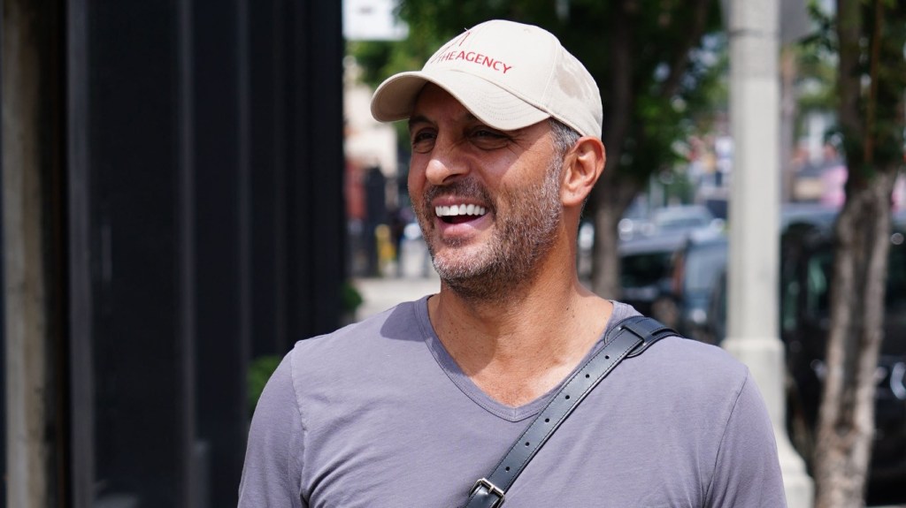 Mauricio Umansky in a grey shirt and white hat, walking down the street smiling