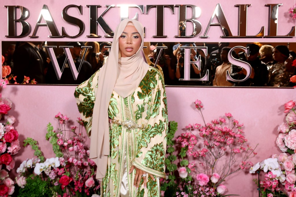 Brittany Renner in a green dress and pink hijab standing in front of the Basketball Wives logo