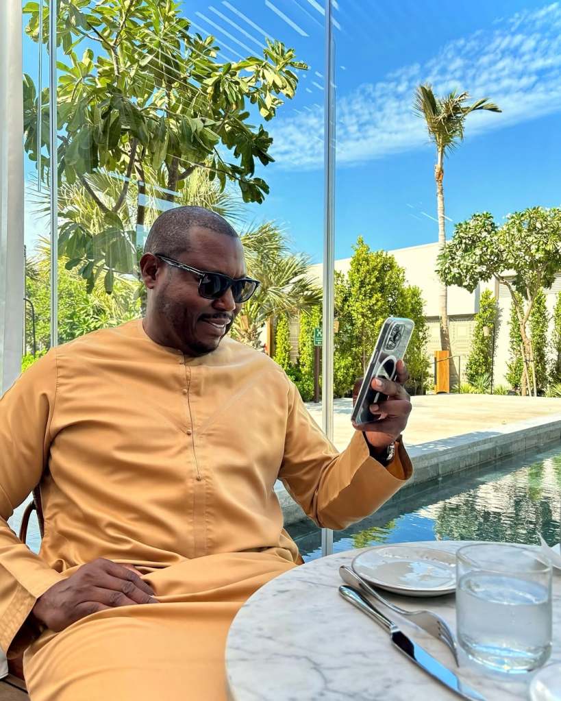 Simon Guobadia wearing orange and looking at his iPhone while sitting outside near a pool