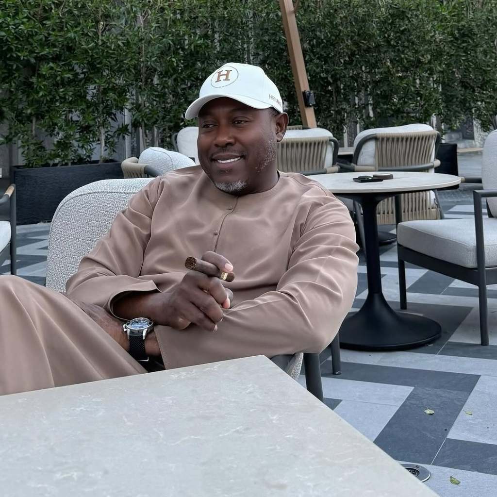 Simon Guobadia sitting at a table and smoking a cigar