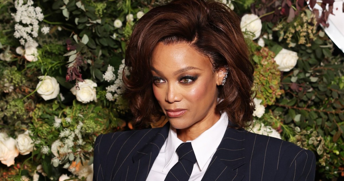 Tyra Banks in a suit posing in front of green and white flowers