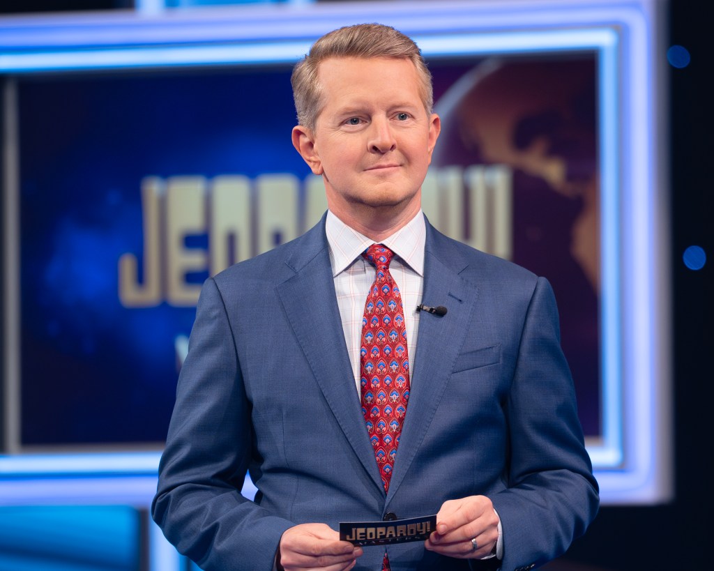 Ken Jennings in a blue suit with a red tie on the set of Jeopardy!