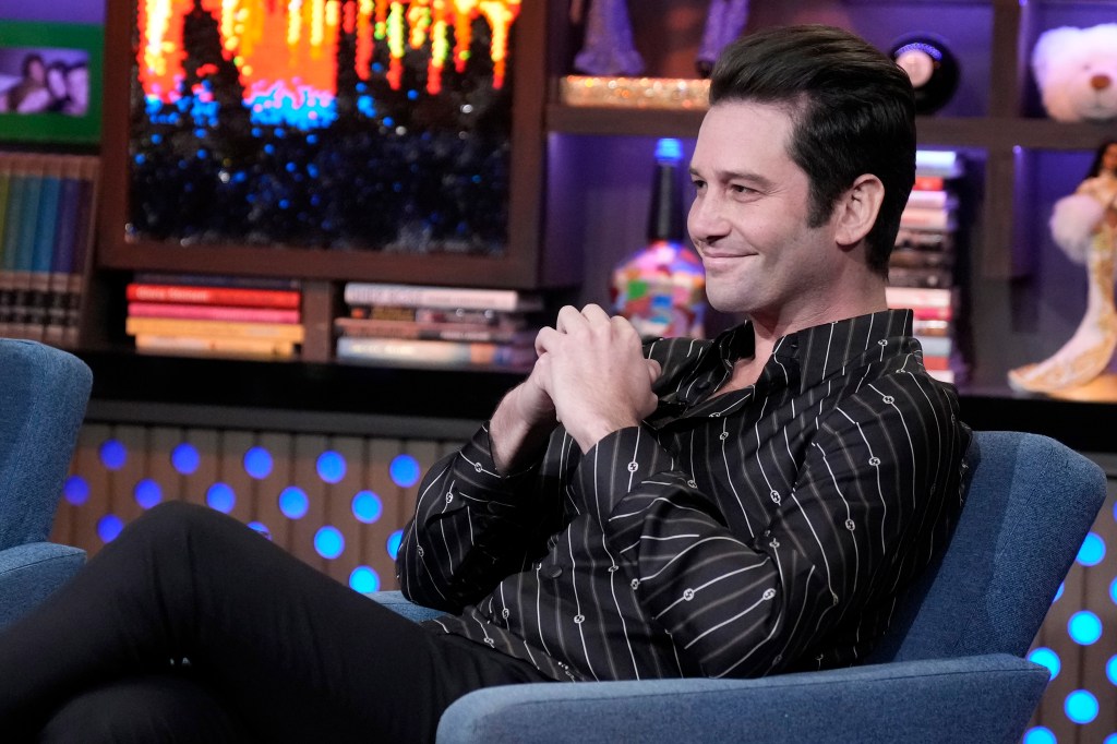 Josh Flagg in a black and white shirt sitting with his hands folded on Watch What Happens Live