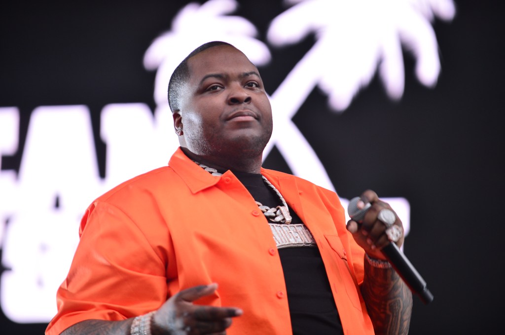 Sean Kingston performing with a microphone in his hand and wearing an orange shirt