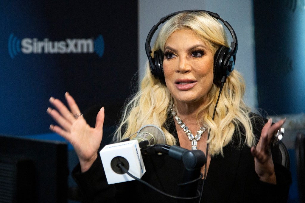 Tori Spelling emoting with her hands and wearing large headphones at SiriusXM studios