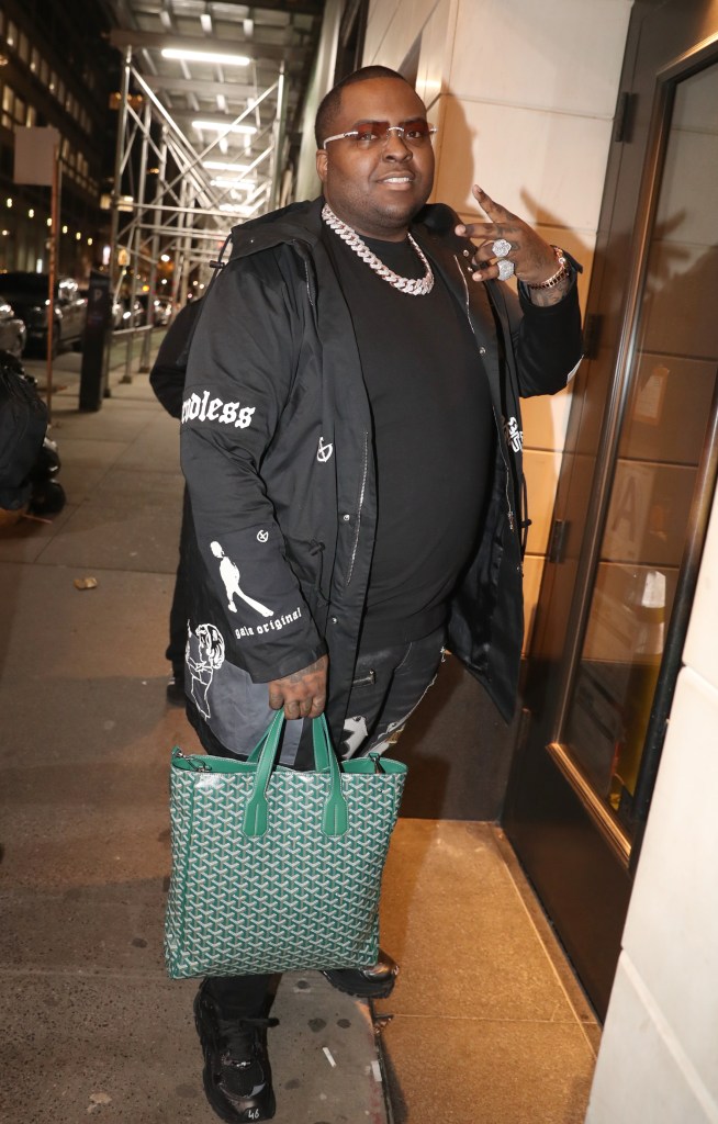 Sean Kingston dressed in all black, throwing up the pink sign, and carrying a green handbag 