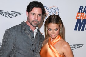 Aaron Phypers in a grey suit posing with Denise Richards, who is wearing an orange dress and looking down