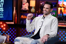 Carl Radke in a white button down shirt raising his fist on Watch What Happens Live