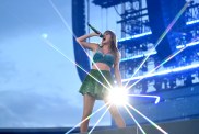 Taylor Swift on stage in a green and blue sparkly outfit, with a large burst of light glimmering off of her