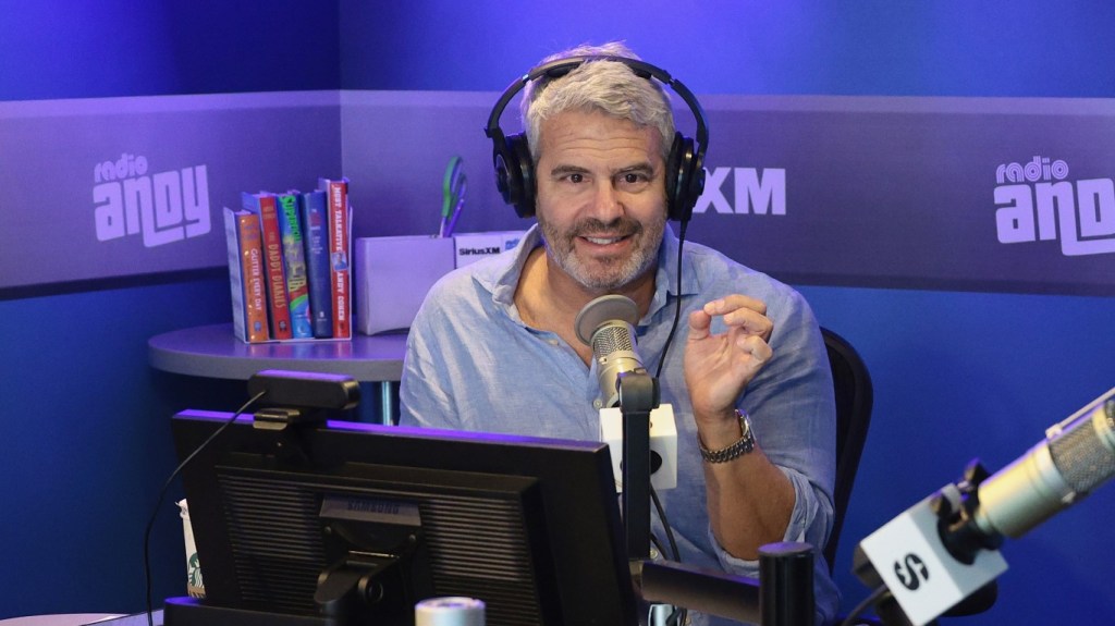 Andy Cohen with headphones in a blue shirt while recording a radio show