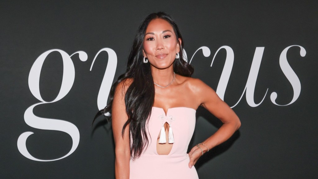 Katie Ginella in a pink dress posing with her hands on her hips