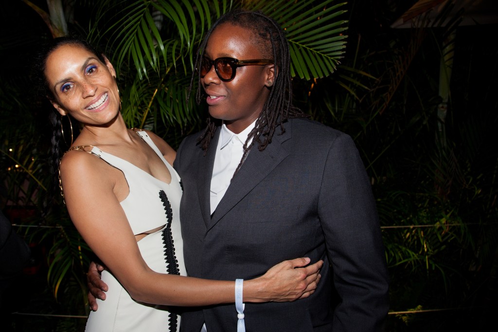 Racquel Chevremont in a white dress holding onto Mickalene Thomas, who is wearing a grey suit