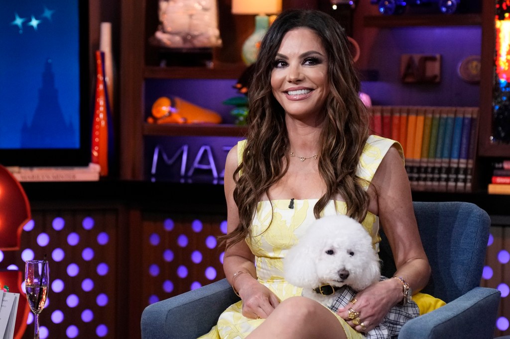 Adriana de Moura in a yellow dress, holding a white dog on Watch What Happens Live