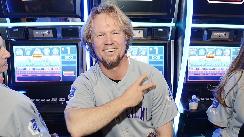Kody Brown in a baseball jersey sitting in front of a slot machine