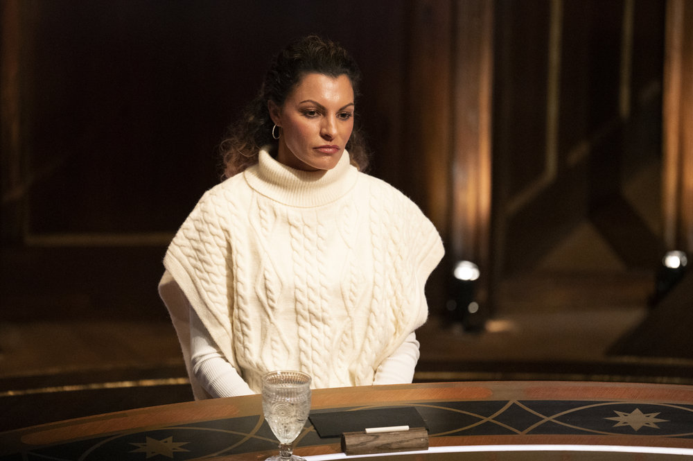 Stephenie LaGrossa in a white sweater looking down at the round table on Traitors Season 1 