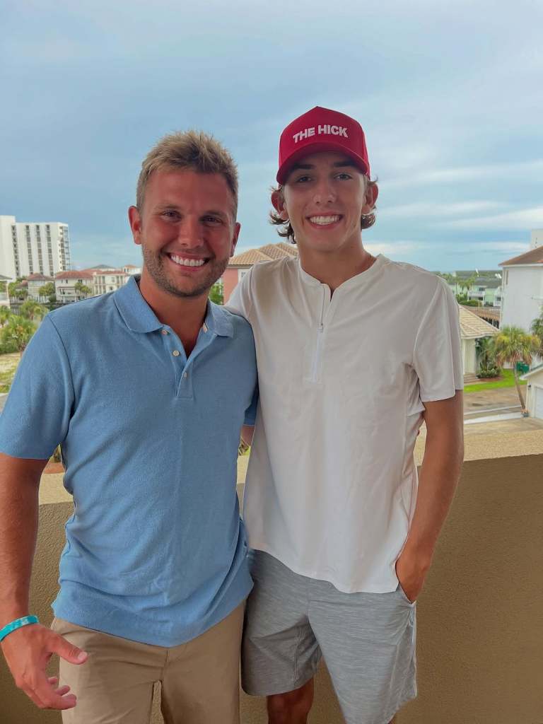 Chase Chrisley in a blue polo shirt posing with Grayson Chrisley, who is wearing a white shirt and red hat
