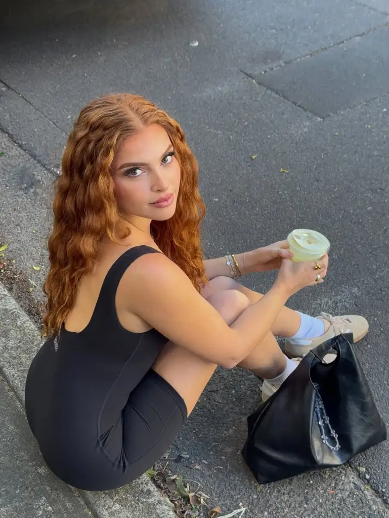 Chanse Corbi sitting on a curb in a black leotard, holding a matcha 