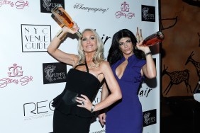 Kim D in a black dress posing with Teresa Giudice in a blue dress; they're both holding up bottles of alcohol