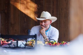 Steve Mcbee Sr sitting at a table full of food, posing with his hand on his chin and wearing a white cowboy hat
