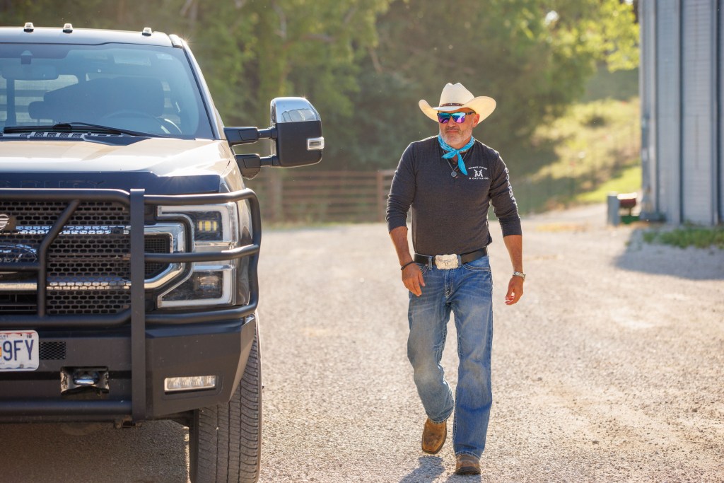 Steve McBee in jeans and a cowboy hat, walking next to a truck