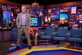 Andy Cohen in a brown suit standing with his legs spread apart in the Watch What Happens Live clubhouse