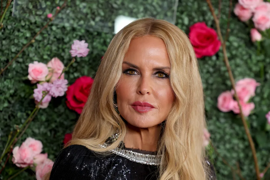 RHOBH's Rachel Zoe in a black dress posing in front of pink and red flowers