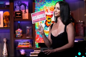 Scheana Shay wearing black on Watch What Happens Live, holding up a red sign that says "Disagree"