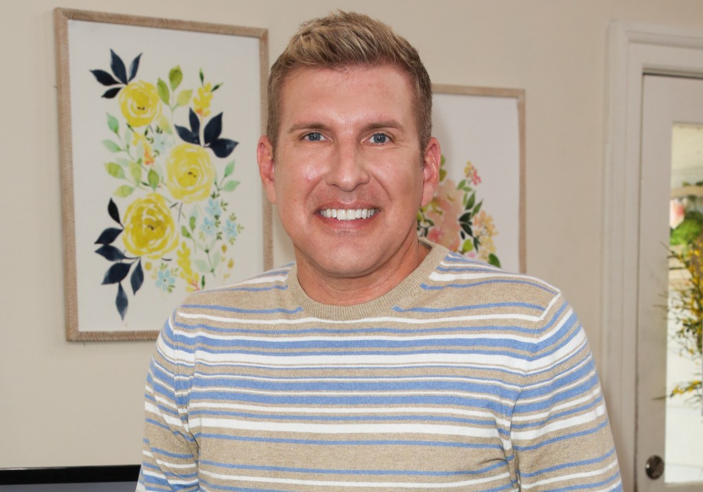 Todd Chrisley in a striped sweater posing in front of floral artwork