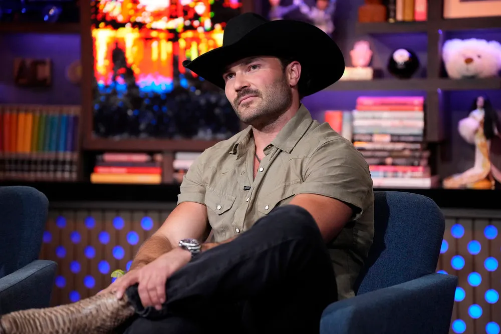 Steven McBee Jr. in a green shirt and black cowboy hat, sitting with his legs crossed on Watch What Happens Live