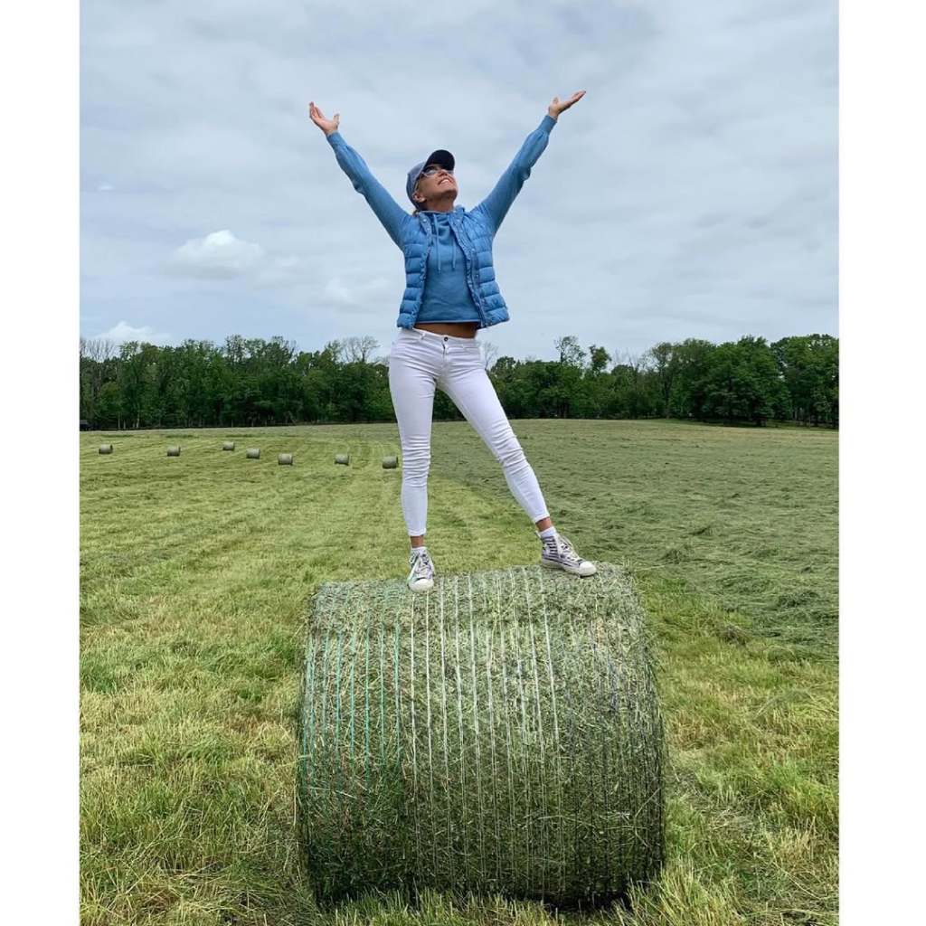 Yolanda Hadid standing on top of a hay bale with her hands up to the sky