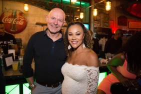 Michael Darby and a pregnant Ashley Darby posing together in front of a bar