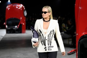 Yolanda Hadid walking in a fashion show in a white blazer, and there are red cards flipped upside down in the background