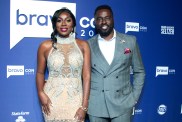 Wendy Osefo in a white gown posing at BravoCon 2022 with Eddie Osefo, who is wearing a grey suit.