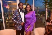Wendy and Eddie Osefo posing in purple outfits in front of a window overlooking Los Angeles