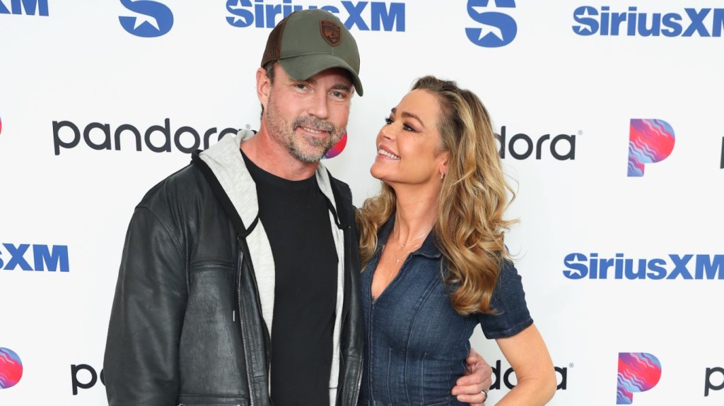 Denise Richards in a denim jumpsuit looking up at Aaron Phypers, who is wearing a leather jacket at SiriusXM