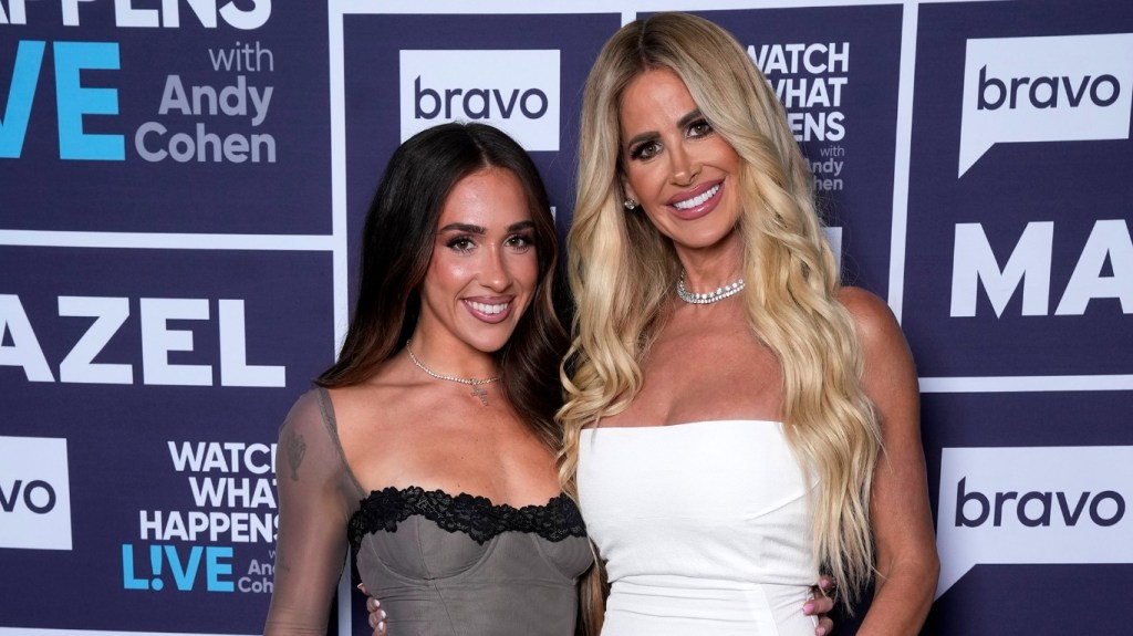 Kim Zolciak, in a white dress, posing with Ariana Biermann, in a grey dress, while backstage at Watch What Happens Live