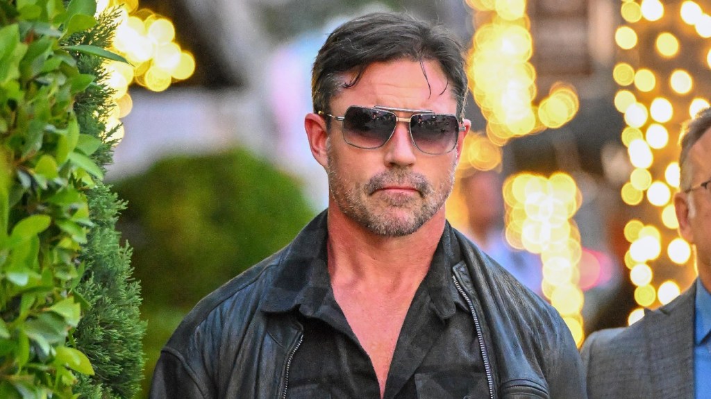 Aaron Phypers walking down a sidewalk in black shades and a leather jacket