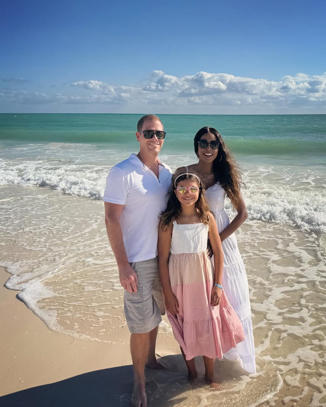 Stacey and Thiemo Rusch posing with their daughter on a beach 