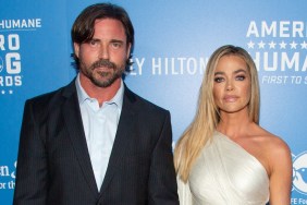 Aaron Phypers in a black suit, posing with Denise Richards, who is wearing a white dress; they're in front of a blue backdrop