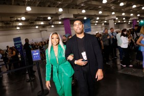 Karen Huger in a green jumpsuit, walking through BravoCon with the help of a security guard