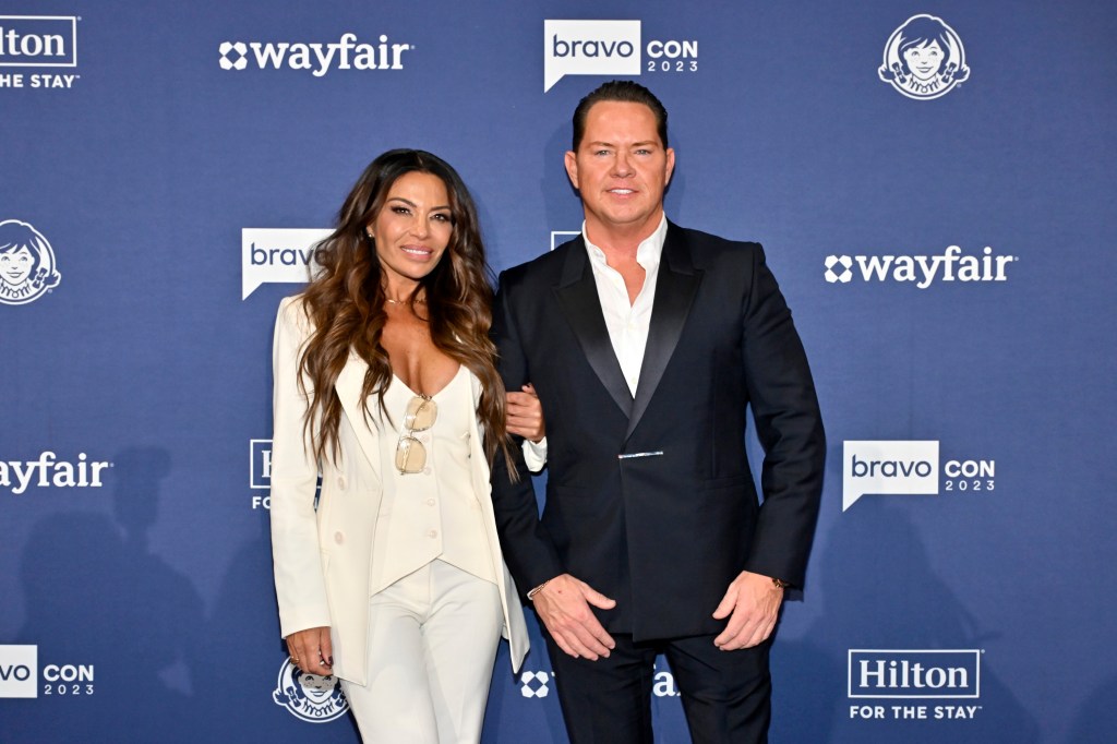 Dolores Catania in a white suit at BravoCon 2023 posing with Paulie Connell in a black suit