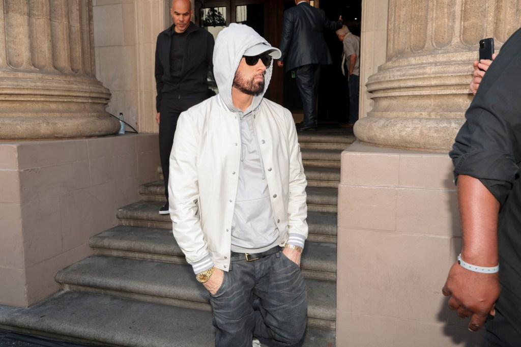 Eminem walking out of a building in a grey hoodie