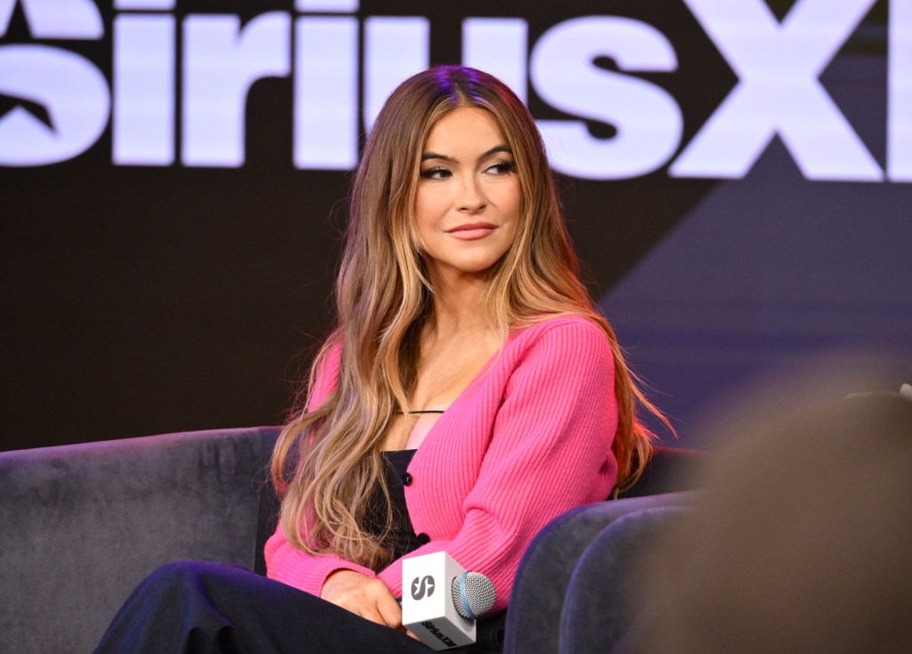 Chrishell Stause in a pink sweater at SiriusXM studios, holding a microphone in her hand