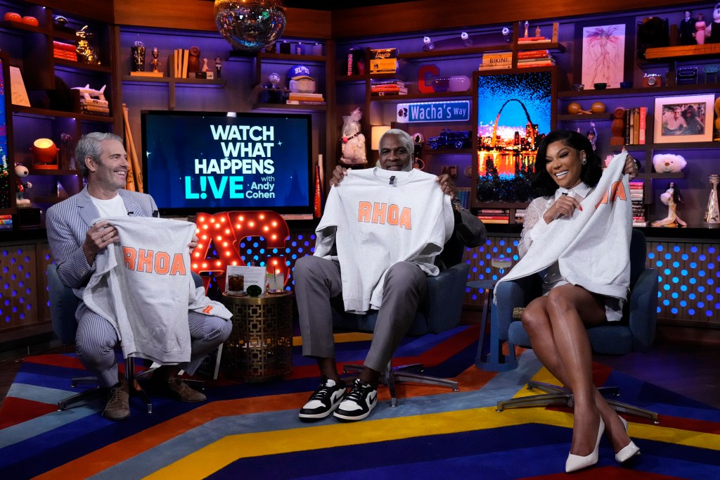 Andy Cohen, Charles Oakley, and Angela Oakley holding up RHOA shirts on Watch What Happens Live