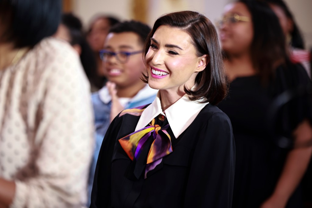 Bronwyn Newport in a black sweater and purple ascot, standing amongst Mary Cosby's congregation