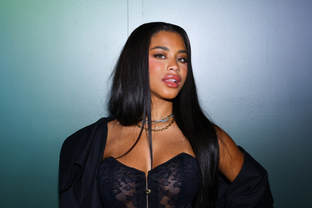 Amaya Espinal posing in a black top and off the shoulder jacket