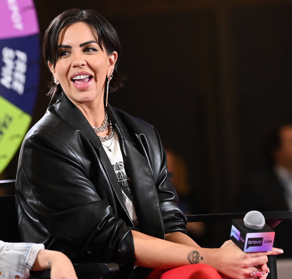 Katie Maloney in a black leather jacket, sitting on stage at BravoCon 