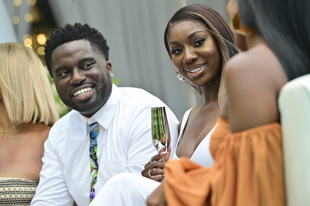Wendy Osefo and Eddie Osefo dressed in white, holding a gold champagne glass