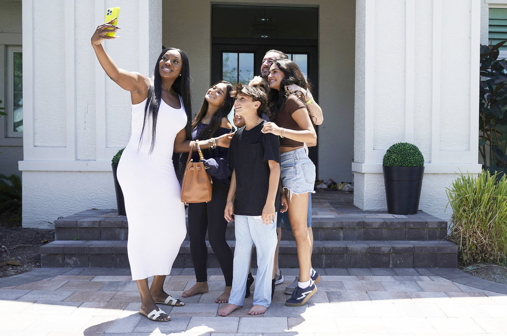 Wendy Osefo in a white dress, posing with her new family on Wife Swap